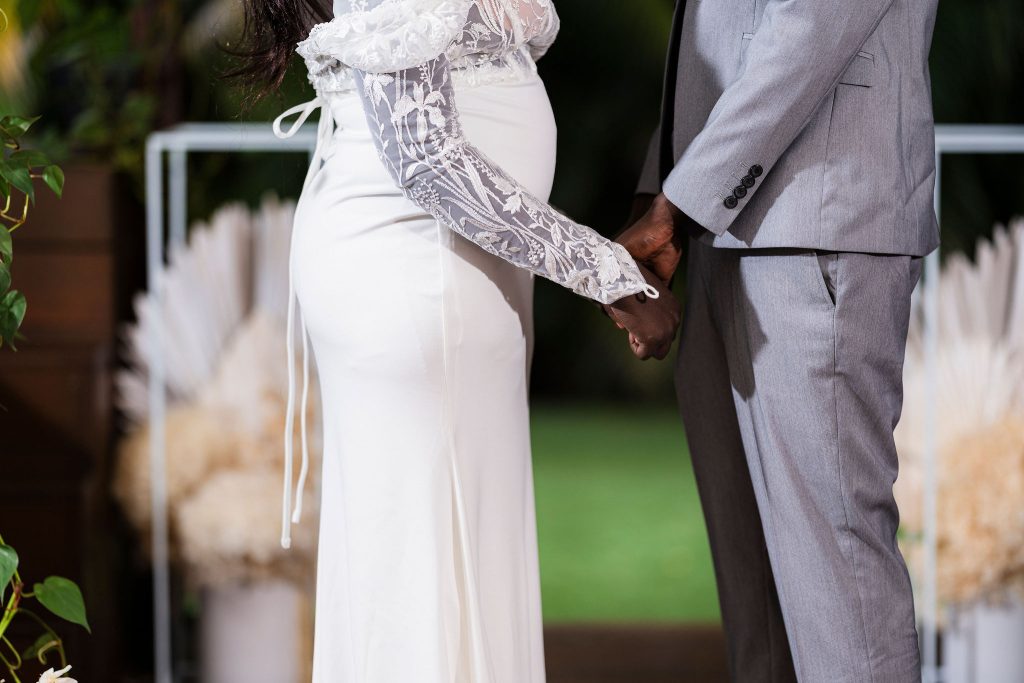 bride and groom holding hands with the brides pregnant tummy in the centre of the image with bride expecting baby